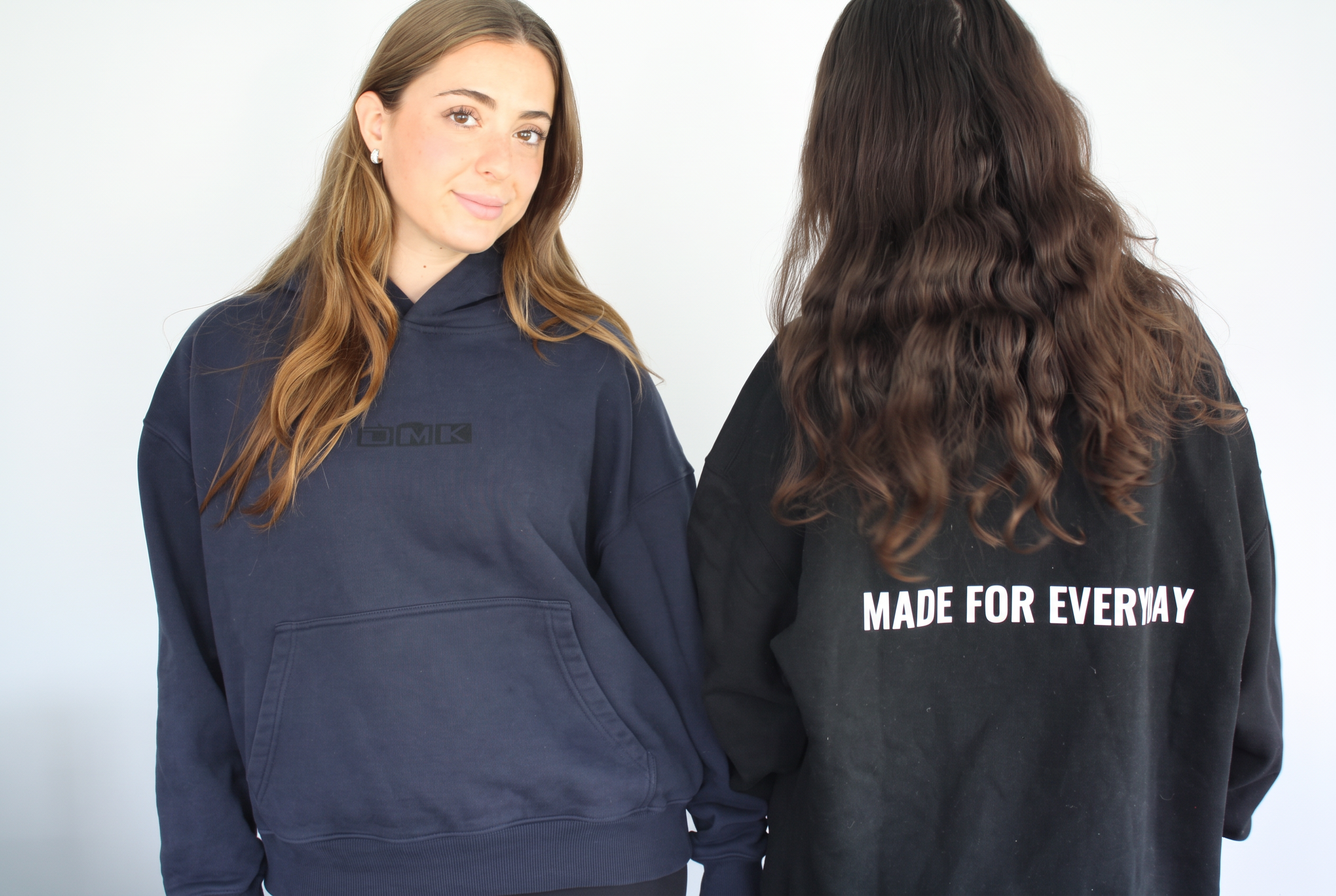 Two models wearing navy and black DMK Studios hoodies